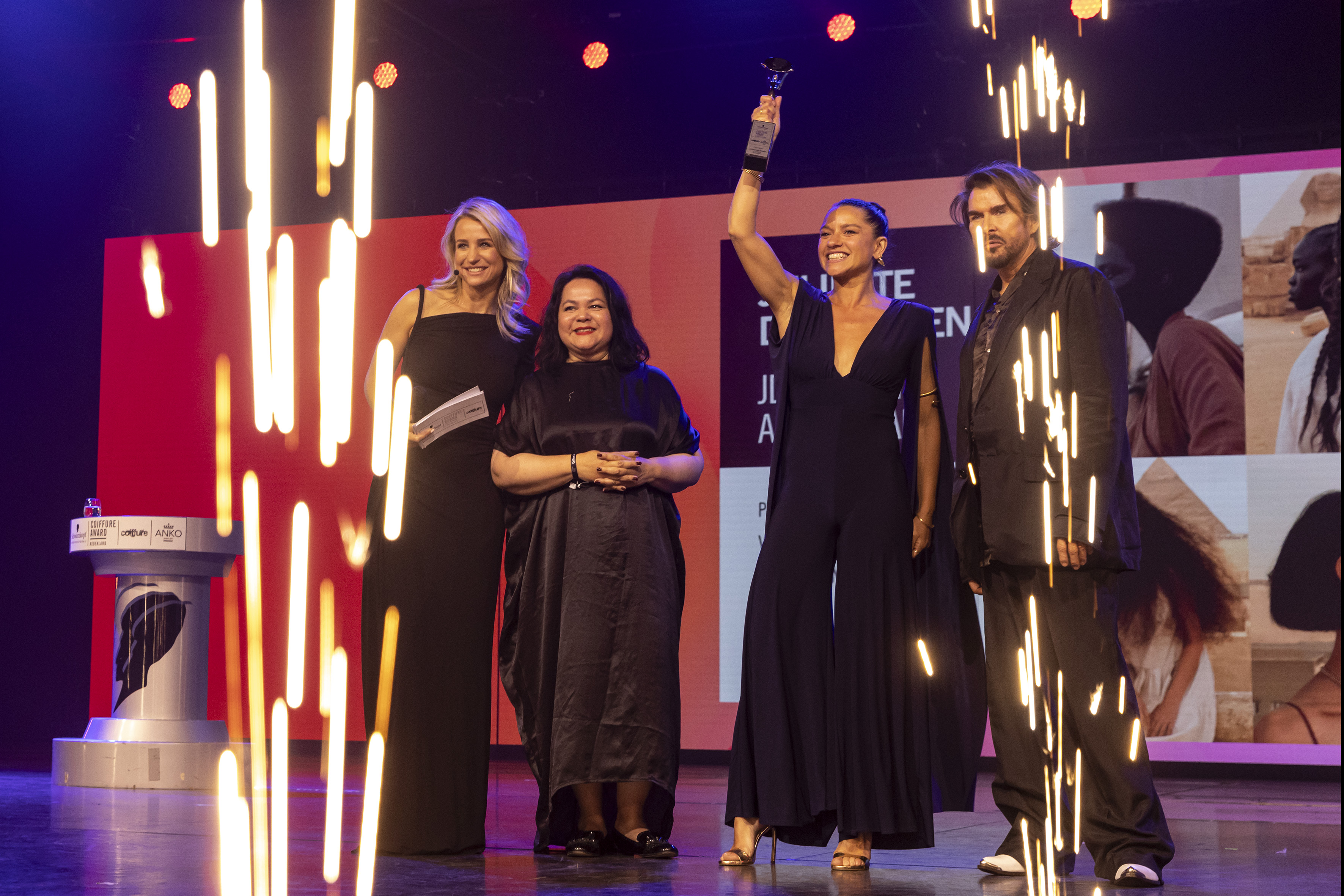 Juliette den Ouden wint een Coiffure Award en houdt de trofee omhoog op het podium